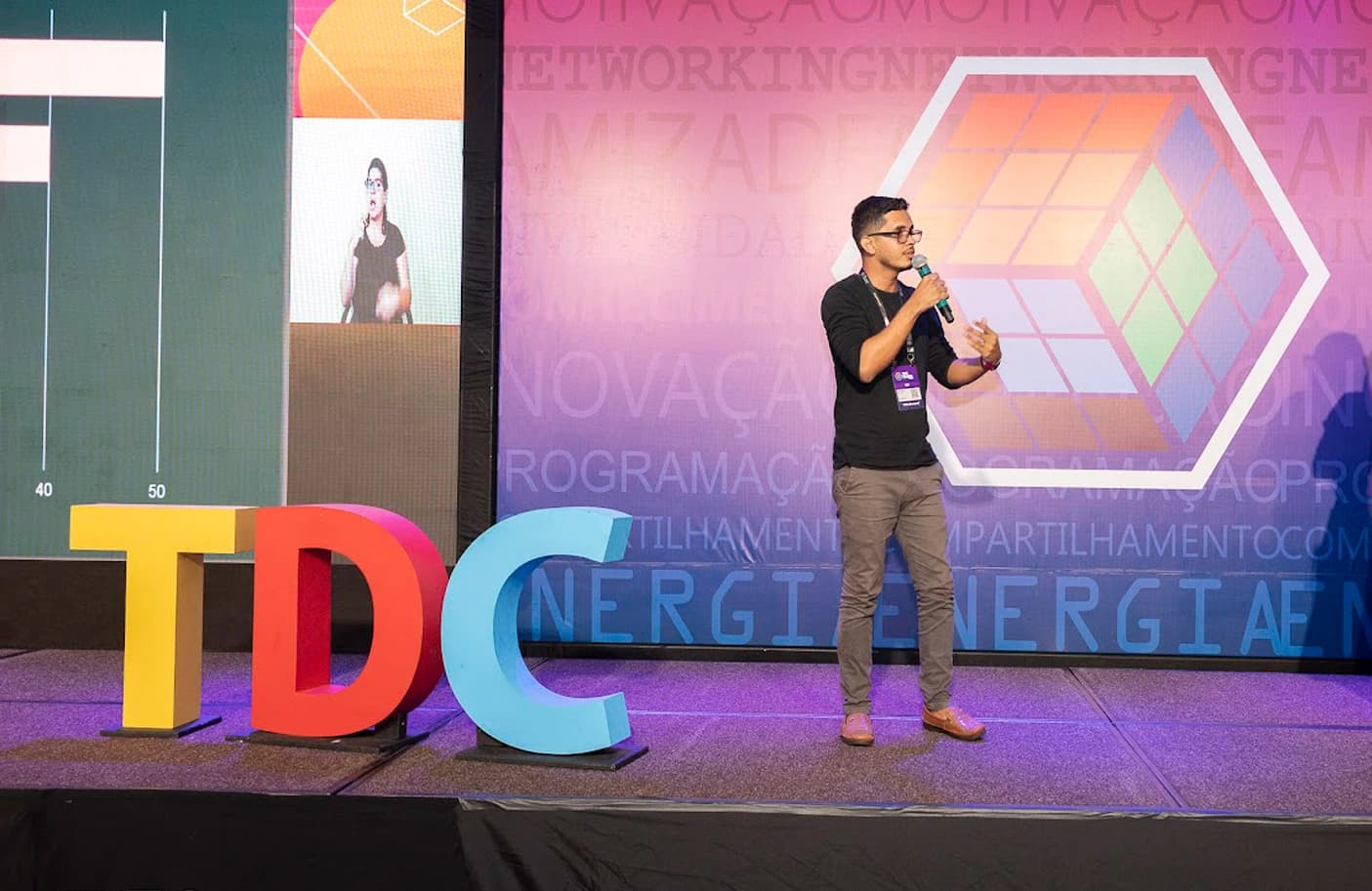 Eduardo Corrêa palestrando no palco do TDC, ao lado das letras coloridas do evento
